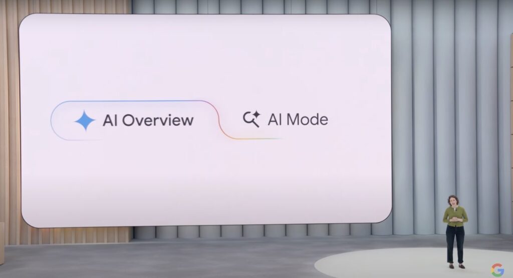 Google employee standing on stage in front of a presentation screen that says AI Overview