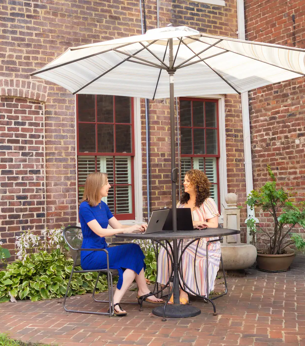 Two Xponent21 team members working on laptops at an outdoor patio table under an umbrella